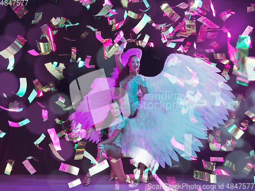 Image of Young female dancers with angel\'s wings in neon light on black background in flying confetti