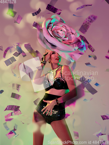 Image of Young female dancer with huge floral hat in neon light on gradient background in flying confetti