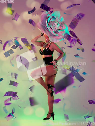 Image of Young female dancer with huge floral hat in neon light on gradient background in flying confetti