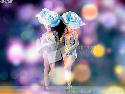 Image of Young female dancers with huge floral hats in neon light on gradient background in flying confetti