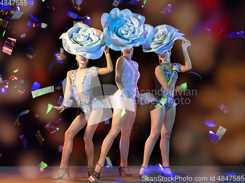 Image of Young female dancers with huge floral hats in neon light on gradient background in flying confetti