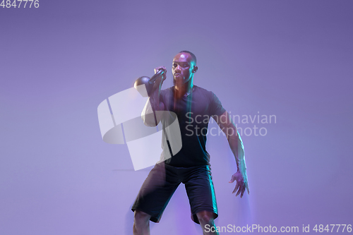 Image of Young african-american bodybuilder training over purple background in neon, mixed light