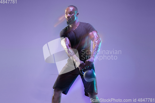 Image of Young african-american bodybuilder training over purple background in neon, mixed light