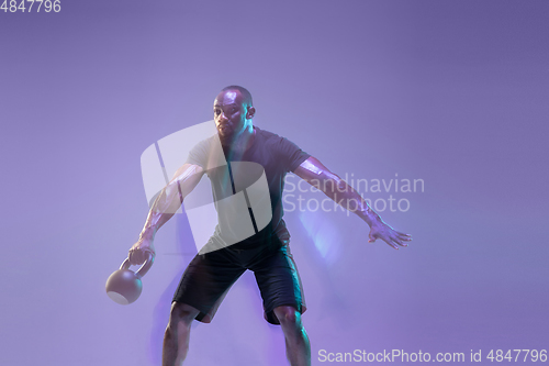 Image of Young african-american bodybuilder training over purple background in neon, mixed light