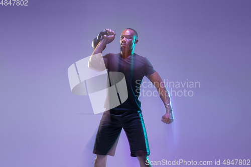 Image of Young african-american bodybuilder training over purple background in neon, mixed light