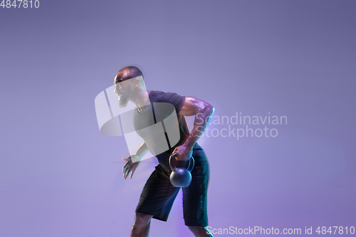 Image of Young african-american bodybuilder training over purple background in neon, mixed light