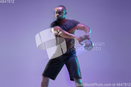 Image of Young african-american bodybuilder training over purple background in neon, mixed light