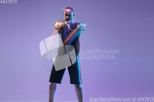 Image of Young african-american bodybuilder training over purple background in neon, mixed light