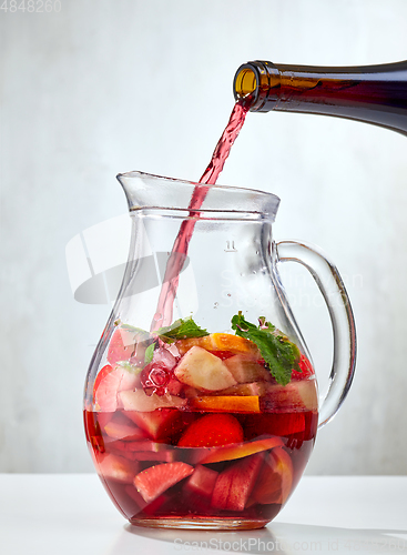 Image of red wine pouring into jug of cutted fruits