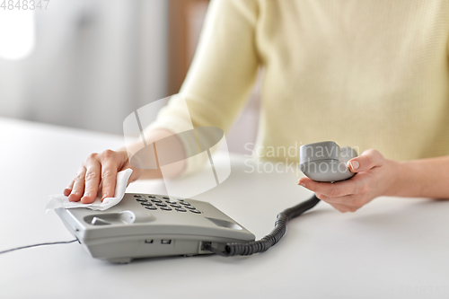 Image of close up of woman cleaning desk phone with tissue