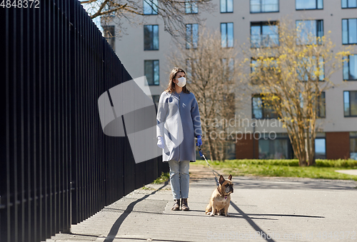 Image of woman in mask and gloves with dog walking in city