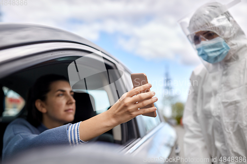 Image of woman in car showing phone to healthcare worker