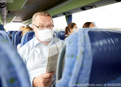 Image of senior man in mask reading newspaper in travel bus