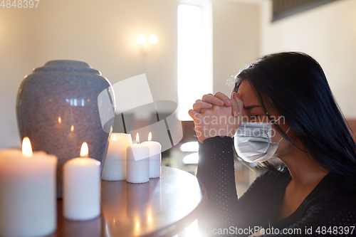 Image of sad woman in mask praying at funeral in church