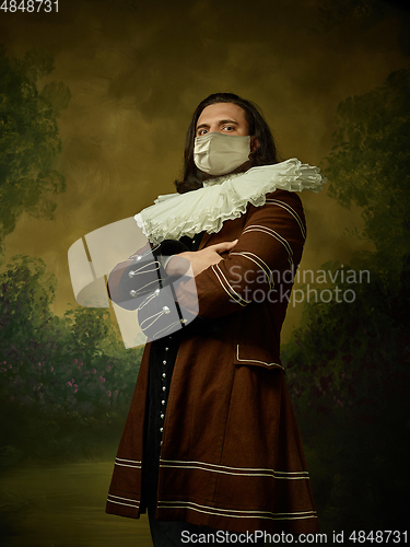 Image of Young man as a medieval knight on dark background wearing protective mask against coronavirus