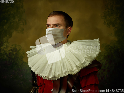 Image of Young man as a medieval knight on dark background wearing protective mask against coronavirus