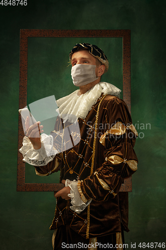 Image of Young man as a medieval knight on dark background wearing protective mask against coronavirus