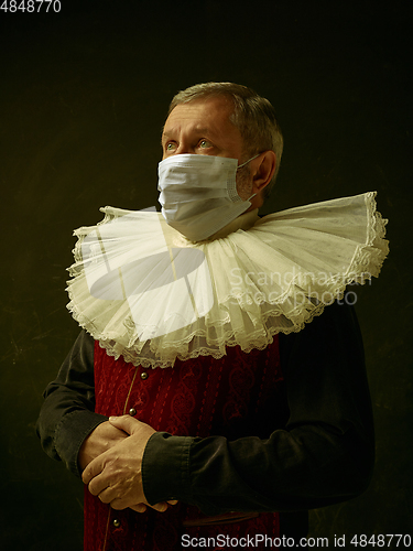 Image of Senior man as a medieval knight on dark background wearing protective mask against coronavirus