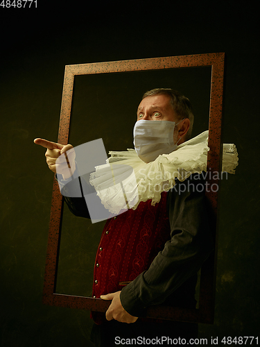 Image of Senior man as a medieval knight on dark background wearing protective mask against coronavirus