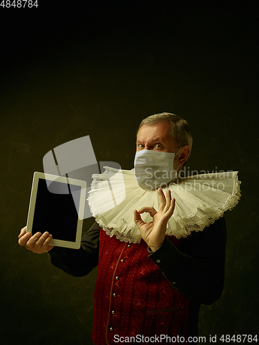 Image of Senior man as a medieval knight on dark background wearing protective mask against coronavirus