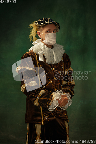 Image of Young man as a medieval knight on dark background wearing protective mask against coronavirus