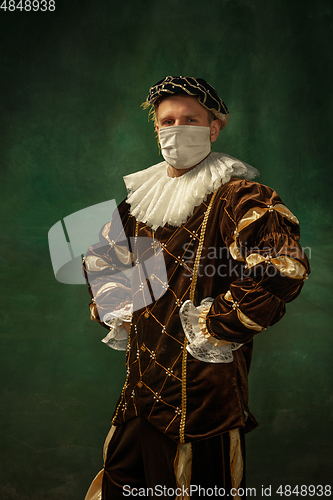 Image of Young man as a medieval knight on dark background wearing protective mask against coronavirus