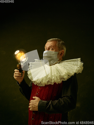 Image of Senior man as a medieval knight on dark background wearing protective mask against coronavirus