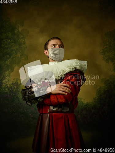 Image of Young man as a medieval knight on dark background wearing protective mask against coronavirus