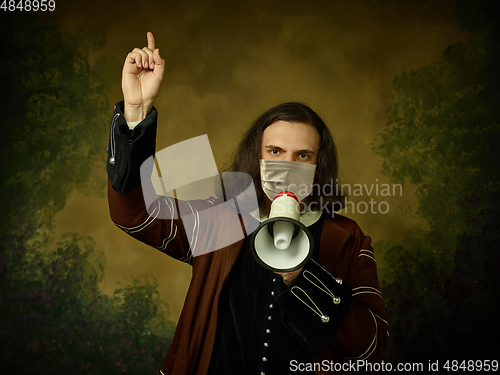 Image of Young man as a medieval knight on dark background wearing protective mask against coronavirus