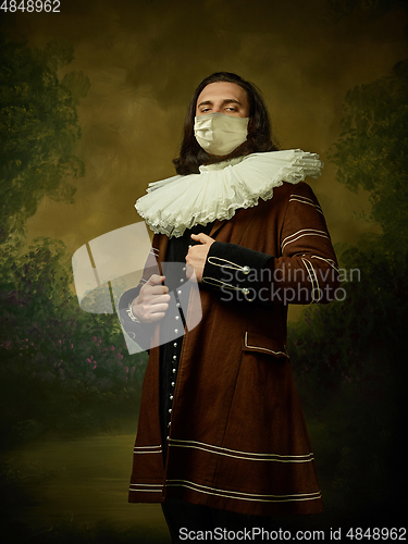 Image of Young man as a medieval knight on dark background wearing protective mask against coronavirus