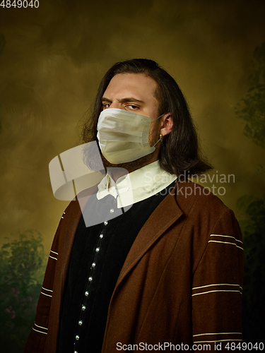 Image of Young man as a medieval knight on dark background wearing protective mask against coronavirus