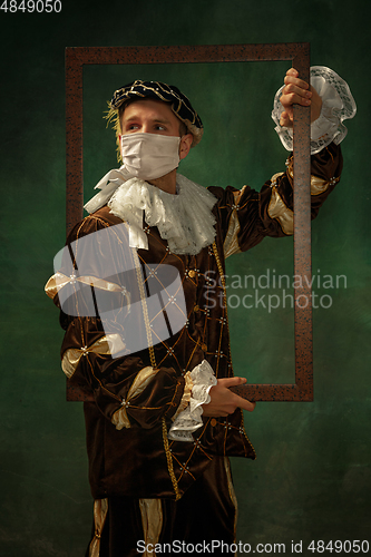 Image of Young man as a medieval knight on dark background wearing protective mask against coronavirus