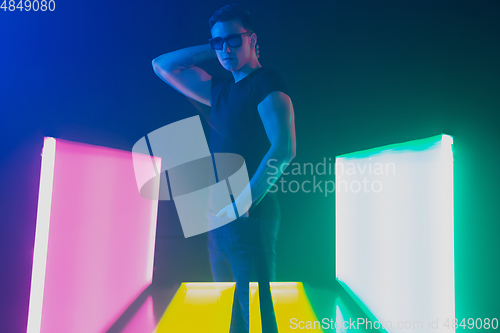Image of Young caucasian man posing stylish in neon light on dark background
