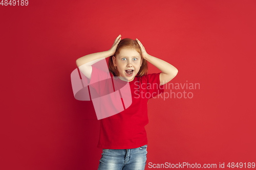 Image of Caucasian little girl portrait isolated on red studio background, emotions concept