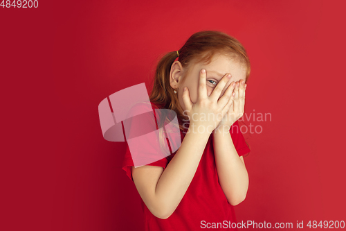 Image of Caucasian little girl portrait isolated on red studio background, emotions concept