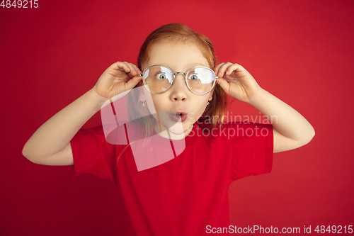 Image of Caucasian little girl portrait isolated on red studio background, emotions concept