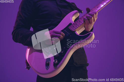 Image of Young caucasian musician playing guitar in neon light on purple background