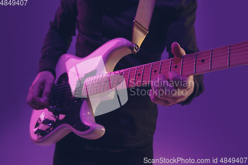 Image of Young caucasian musician playing guitar in neon light on purple background