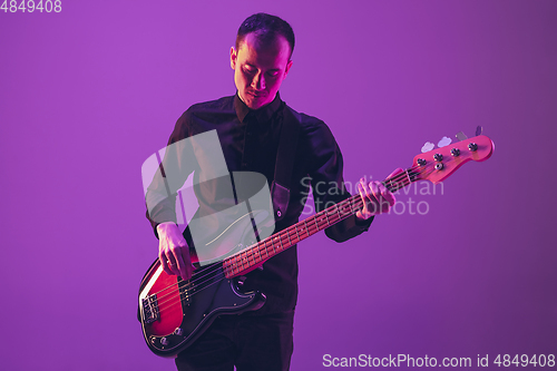 Image of Young caucasian musician playing guitar in neon light on purple background