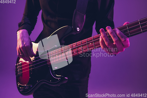 Image of Young caucasian musician playing guitar in neon light on purple background