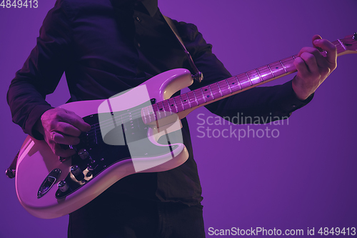 Image of Young caucasian musician playing guitar in neon light on purple background