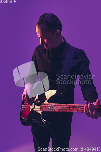 Image of Young caucasian musician playing guitar in neon light on purple background
