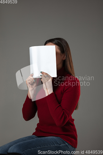 Image of Happy world book day, read to become someone else - woman covering face with book while reading on grey background