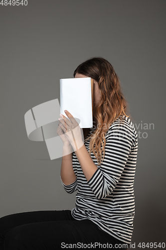 Image of Happy world book day, read to become someone else - woman covering face with book while reading on grey background