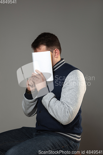 Image of Happy world book day, read to become someone else - man covering face with book while reading on grey background