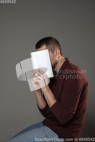 Image of Happy world book day, read to become someone else - man covering face with book while reading on grey background