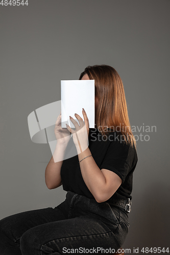 Image of Happy world book day, read to become someone else - woman covering face with book while reading on grey background