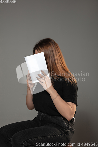 Image of Happy world book day, read to become someone else - woman covering face with book while reading on grey background