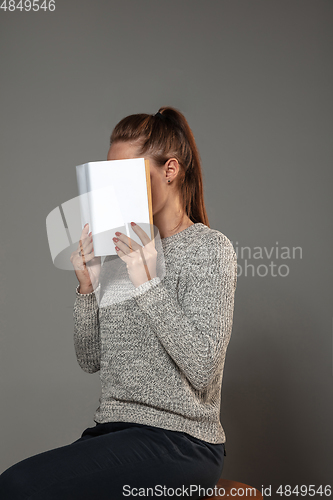 Image of Happy world book day, read to become someone else - woman covering face with book while reading on grey background
