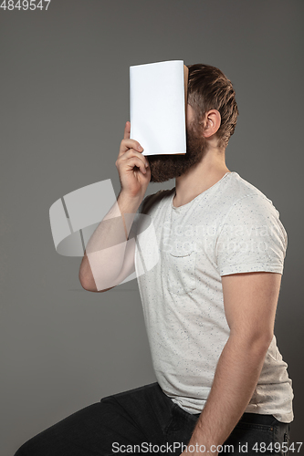 Image of Happy world book day, read to become someone else - man covering face with book while reading on grey background